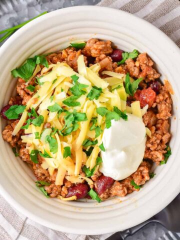 Bowl of dutch oven chili topped with shredded cheese and sour cream.