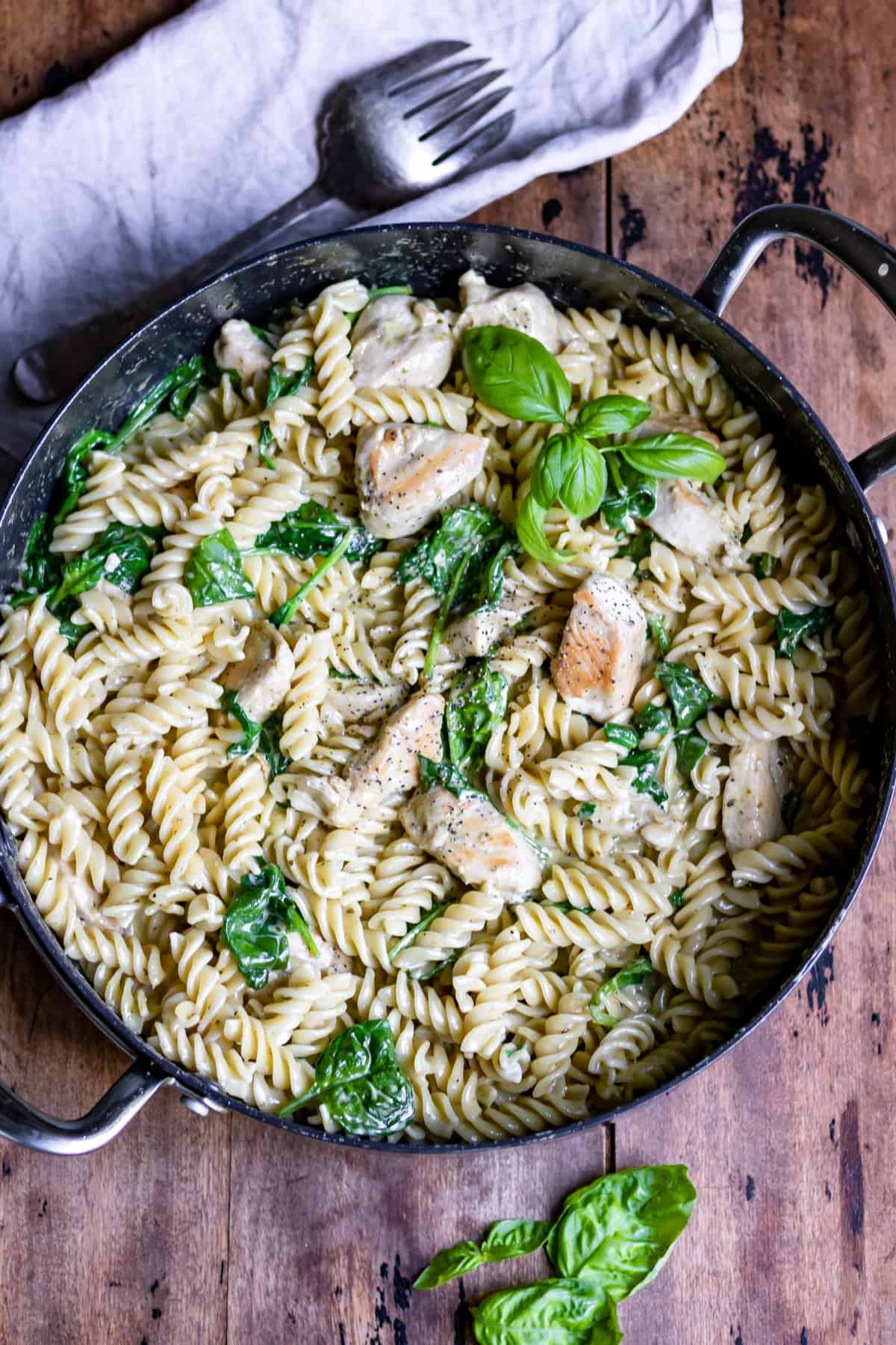 Wooden table with a serving dish of creamy chicken pesto pasta.