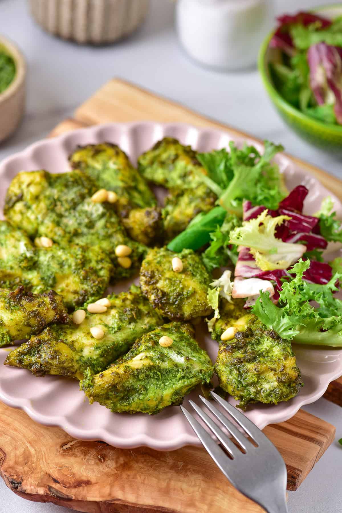 Plate with a pile of basil pesto chicken bites and salad.