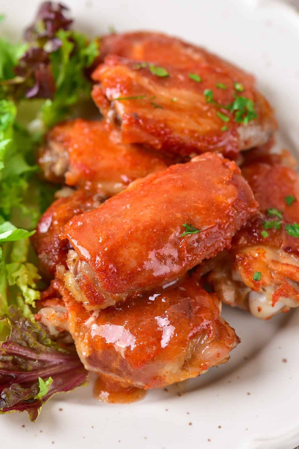 Pile of buffalo bacon wrapped chicken wings on a plate with salad.