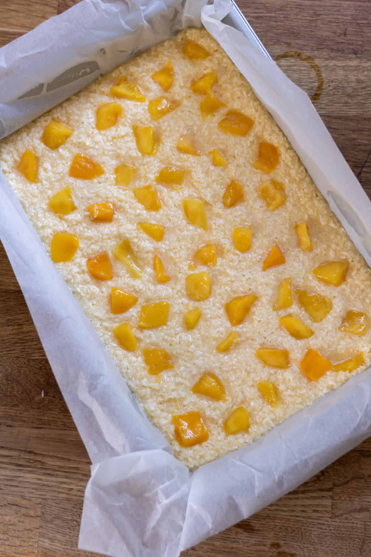 Batter in a pan with mango chunks sprinkled on top.