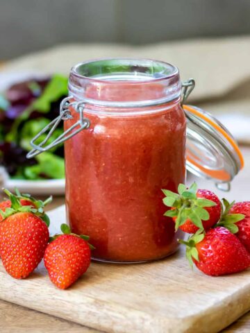 Jar of strawberry vinaigrette on a wooden board next to strawberries.
