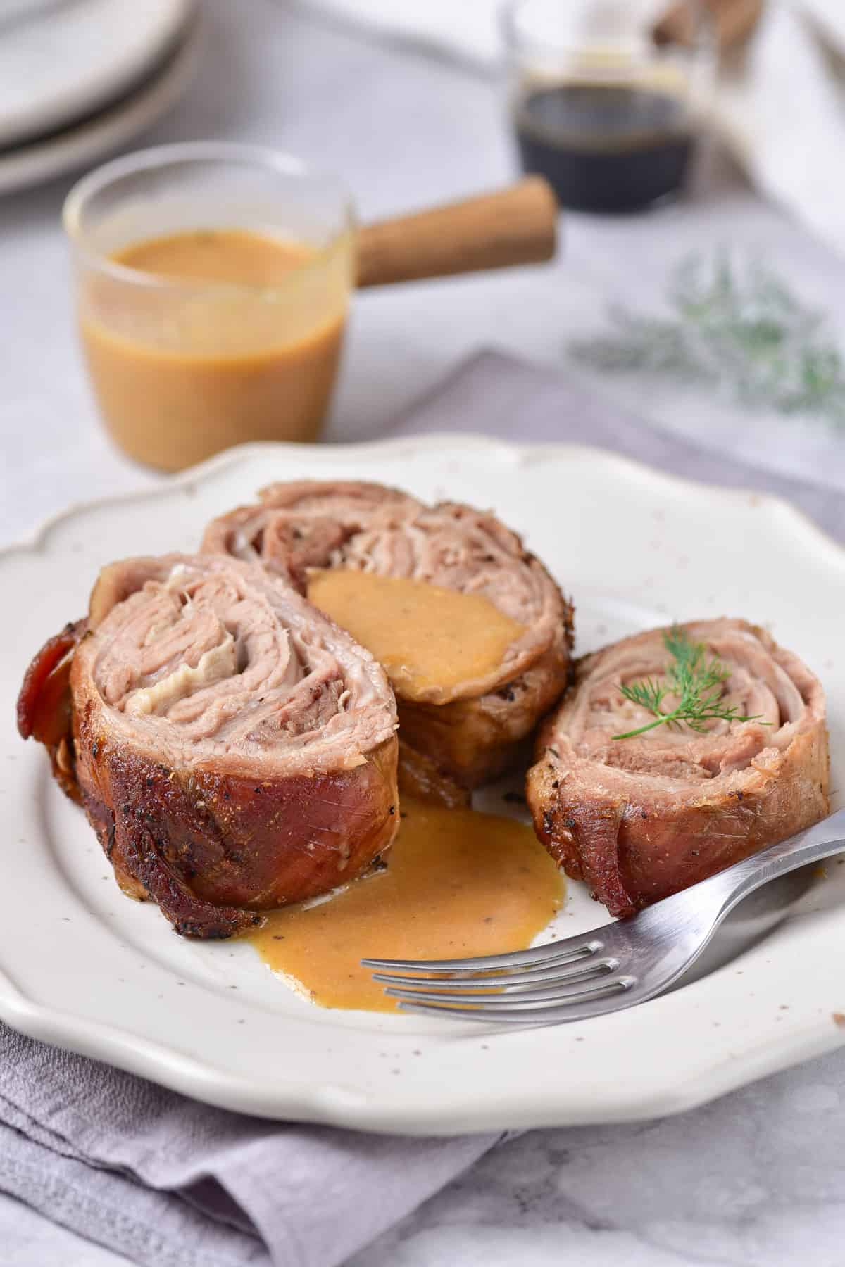 Table with a plate of rolled lamb breast slices, with a jug of gravy.