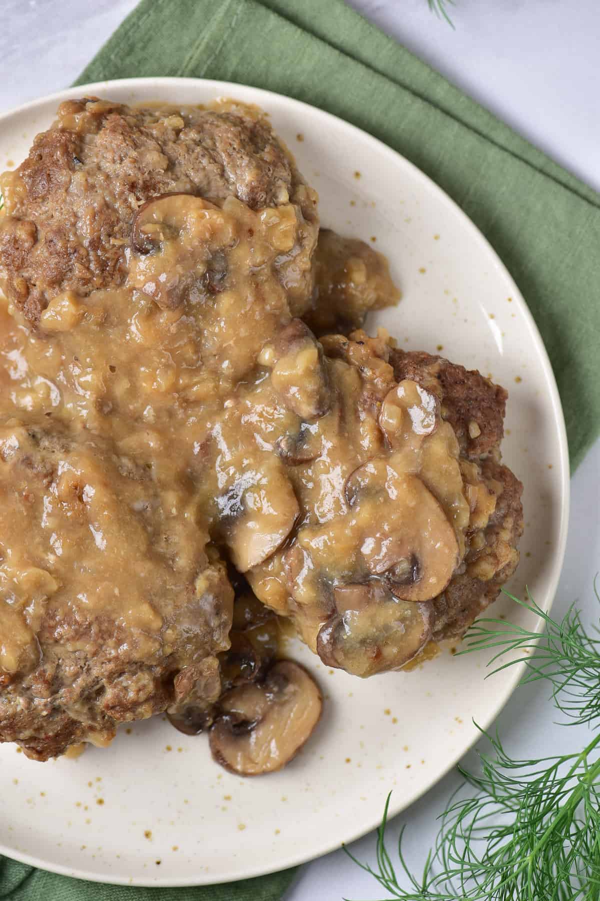 Close up of three salisbury steaks on a serving dish, covered in mushroom gravy.