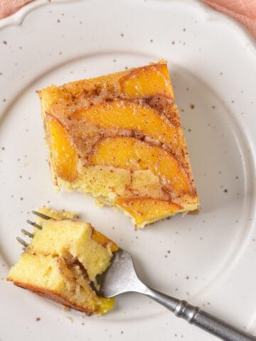 Table with a plate, slice of peach upside down cake, and forkful of cake.