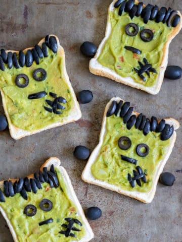 Rows of toast with guacamole plus sliced black olives arranged to look like Halloween Frankensteins.