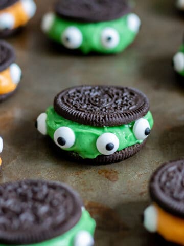 Close up of an Oreo filled with green frosting and dotted around the edge with candy eyes.